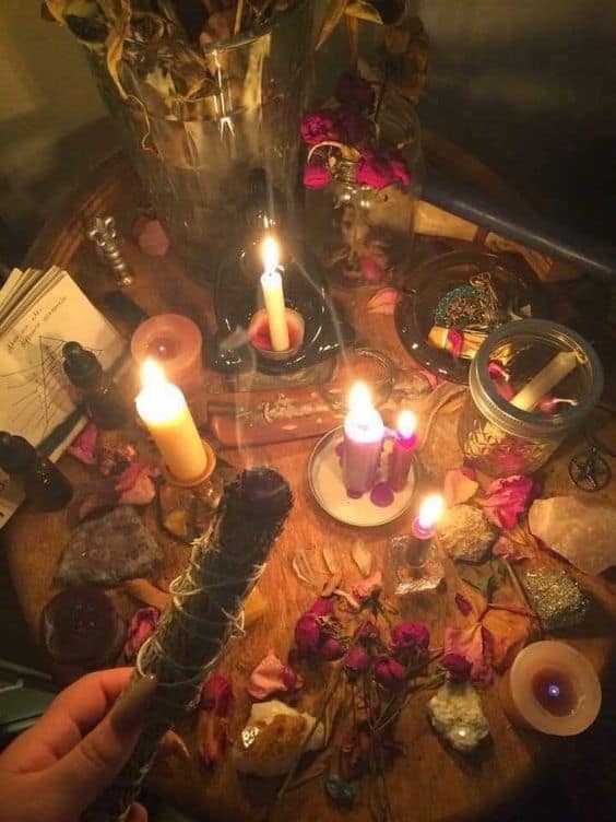 Mesa con velas de diversos colores, flores secas, cristales y palo santo para un ritual de amor